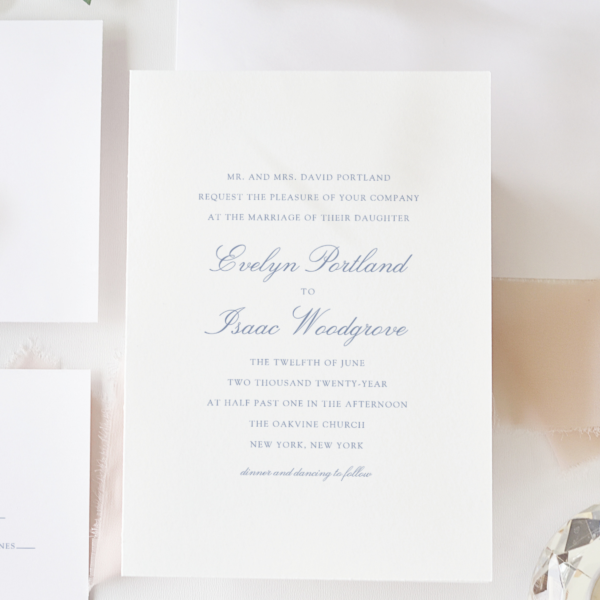 minimal blue wedding invitation next to wedding enclosure cards and botanical flatlay